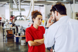 Young woman in workplace with arms crossed getting chastised by male manager